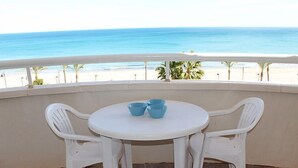 Un balcone con tavolo e due sedie bianche, vista sulla spiaggia.