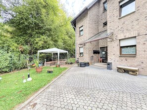 Ein Backsteinhaus mit gepflasterter Terrasse, einem weißen Zelt und einem Garten mit Topfpflanzen.