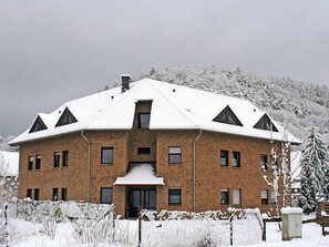 Un grand bâtiment en briques, à plusieurs étages, dont le toit est recouvert de neige et qui possède une entrée centrale.