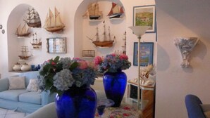 A living room with a blue sofa, two large vases with flowers, and several model ships on the wall. - Casa Bacot - Four Bedroom Villa, Sleeps 8 (Canneto)