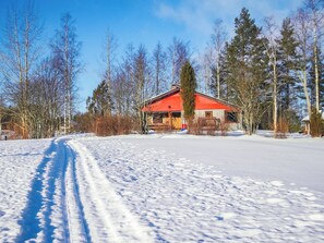 Un paysage enneigé avec une cabane aux toits rouges, entourée d’arbres.