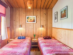 Una habitación con dos camas, paredes de madera, un cuadro y dos lámparas fijadas a la pared.