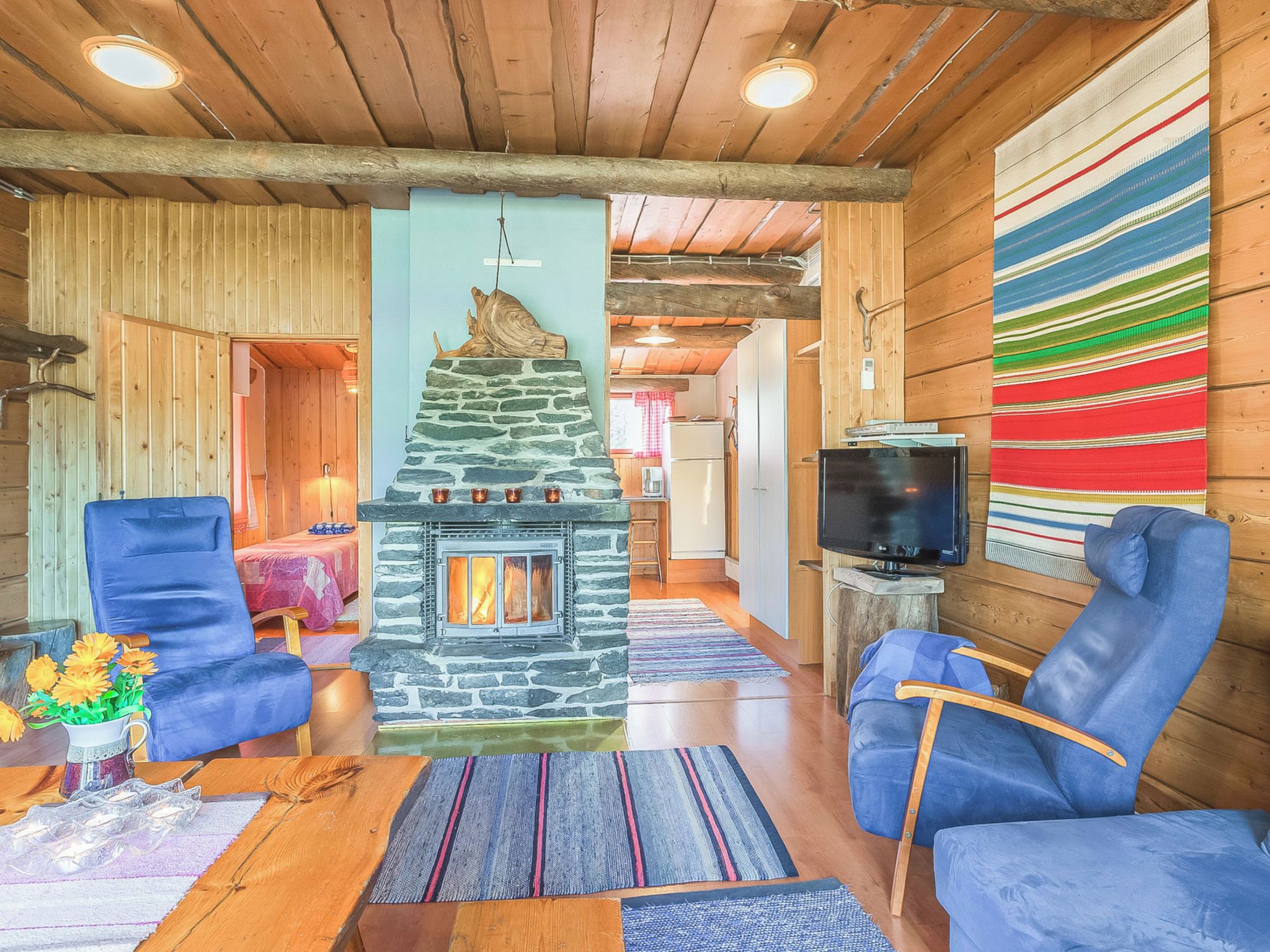A cozy interior with a stone fireplace, blue armchairs, a television, and a colorful striped rug.