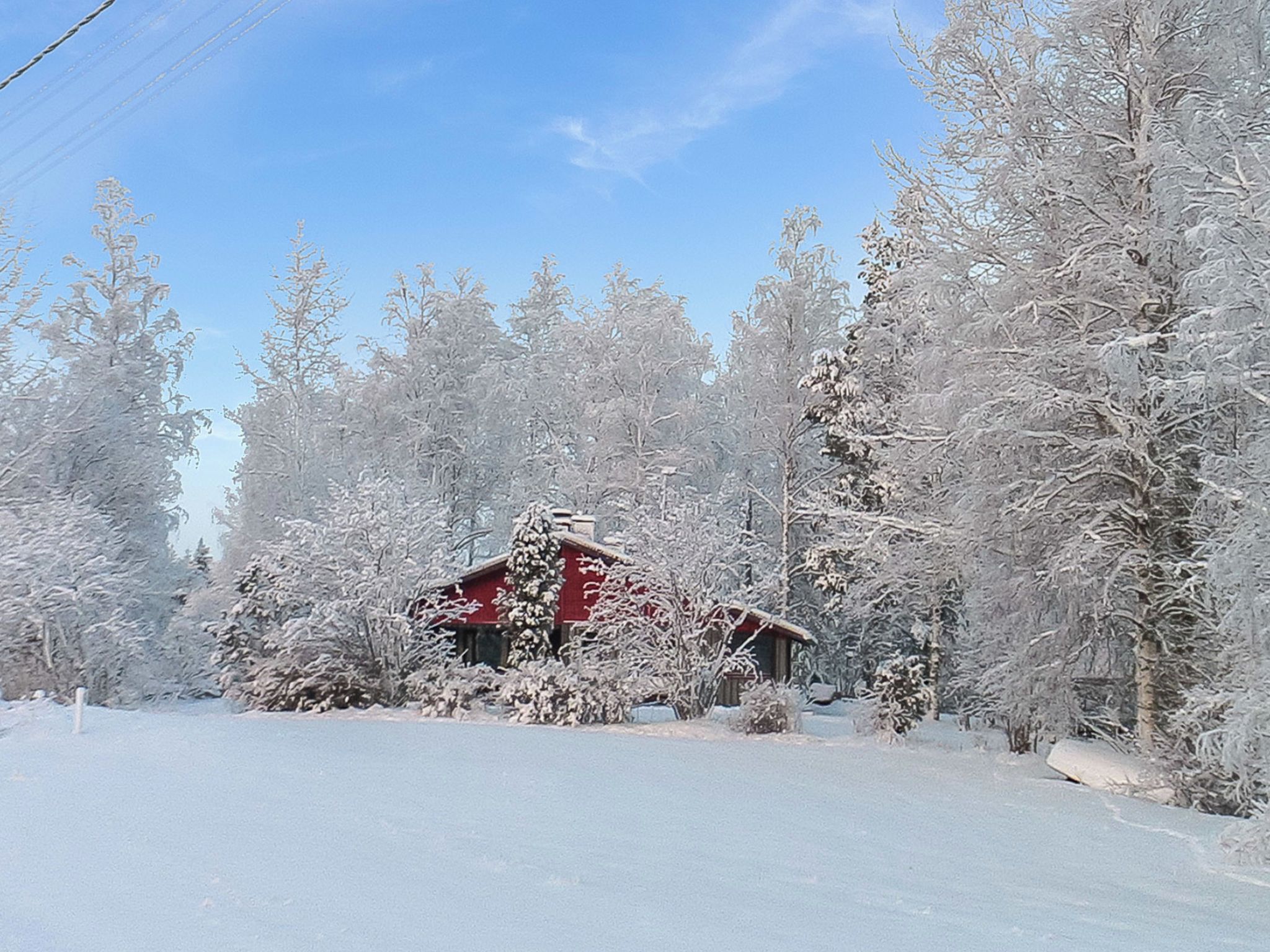 A snow-covered landscape with a red building, surrounded by trees.