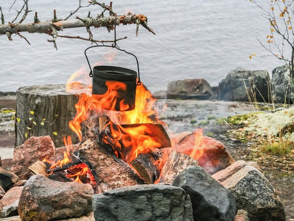 Una fogata con una olla encima, rodeada de rocas y un tocón de madera.