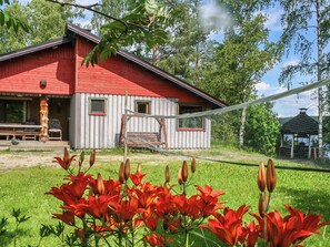 A red wooden house with a porch, surrounded by green grass and trees.