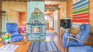 Een gezellig cabin interieur met een stenen open haard, blauwe fauteuils en een kleurrijke wandhanger met strepen.