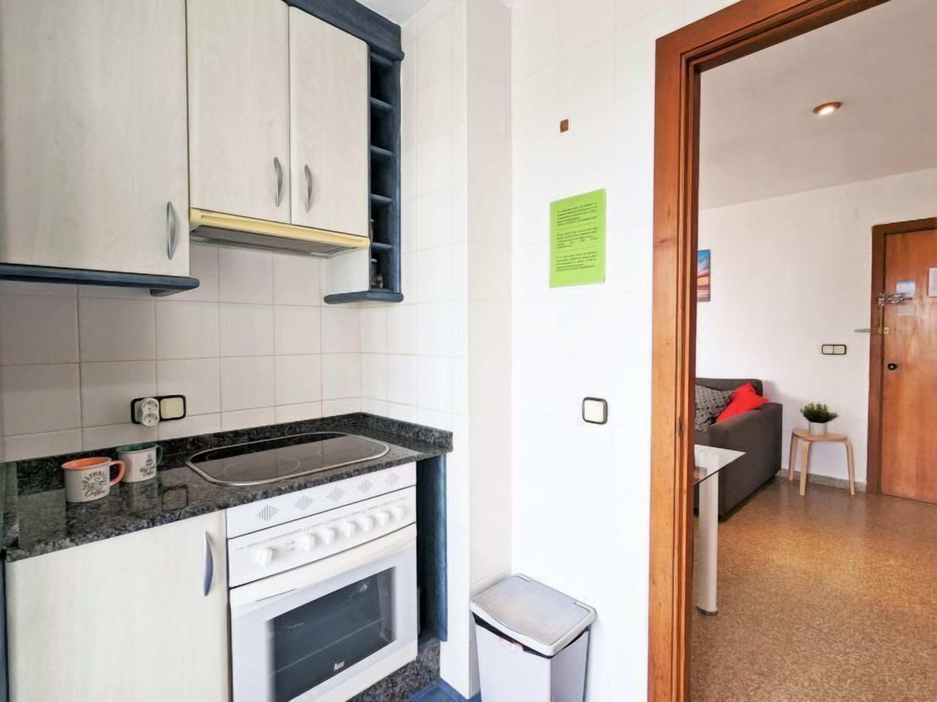 A compact kitchen with white cabinets, a built-in oven, and a granite countertop.