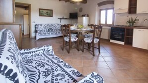 Ein gemütliches Wohnzimmer mit einer gemusterten Couch, einem Esstisch für vier Personen und einer Küchenzeile mit weißen Schränken und einem Herd.
