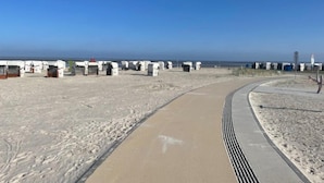 Een zandstrand met een boogvormig pad dat leidt naar een rij witte gebouwen, mogelijk strandhutten, langs de kustlijn.