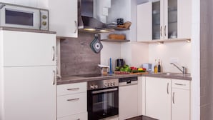 Een moderne keuken met witte kastjes, een inbouwoven, een magnetron en een rvs afzuigkap.