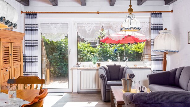 Een gezellige woonkamer met een houten plafond, een eettafel met stoelen, een bank en een raam met gordijnen.