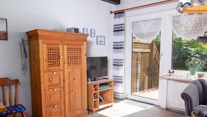 Een gezellige woonkamer met een houten kast, een televisie en een schuifdeur naar een tuin.