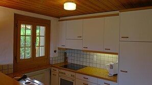 Cocina compacta con armarios de madera, horno integrado y ventana con vista a zonas verdes.