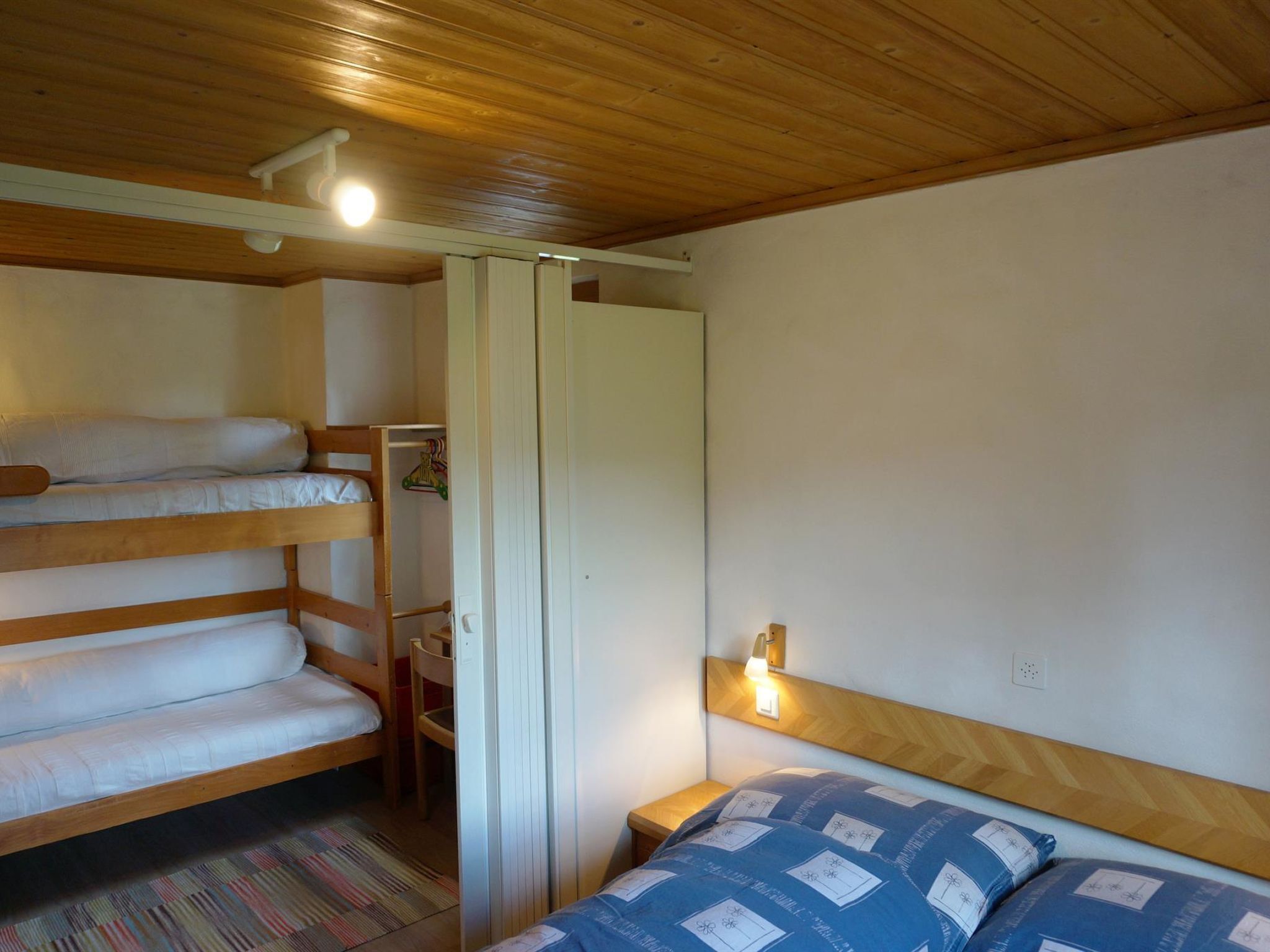 Een kamer met stapelbedden, een klein tafeltje en een nachtkastje met een lamp.