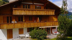 Un chalet de madera de dos pisos con balcones, un porche cubierto y vistas del paisaje circundante.