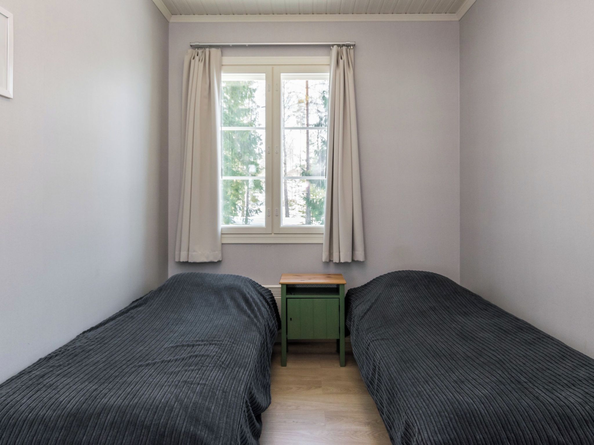 Un dormitorio con dos camas individuales, una mesita y una ventana con cortinas.