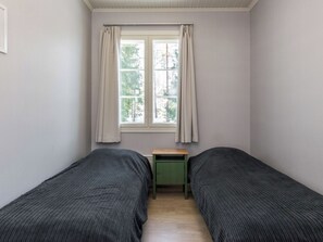 Un dormitorio con dos camas individuales, una mesita y una ventana con cortinas.