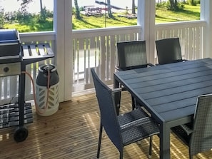 Een terras buiten met een barbecue, een tafel en stoelen.