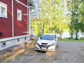 Une voiture blanche est garée devant un bâtiment rouge, avec une allée gravillonnée.