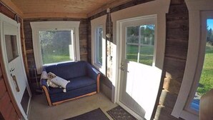 Een gezellige kamer met een blauwe bank, houten wanden en grote ramen.