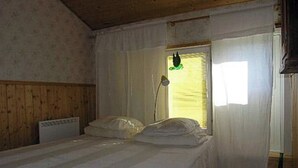 Een enkel bed met witte lakens in een kamer met houten wanden en een raam met dunne gordijnen.