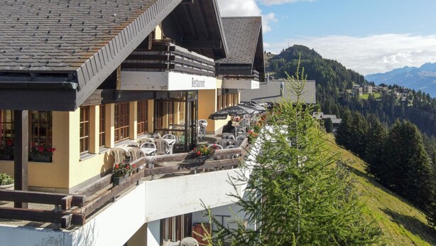 Un ristorante con posti a sedere all'aperto su un pendio, con vista su un paesaggio montuoso.