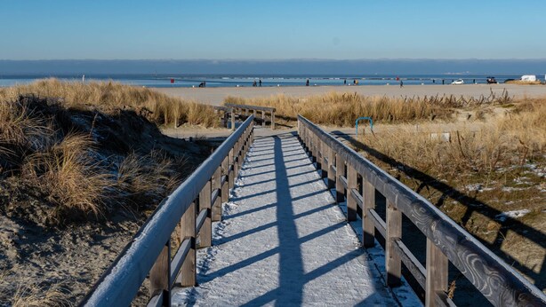 Un paseo marítimo de madera que conduce a una playa, con cielo despejado.