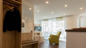 A modern hotel room with a wooden bench, a yellow armchair, a TV, and a large window offering a view of the outside. - Haus Alpenrose by Interhome (Saas-Almagell)
