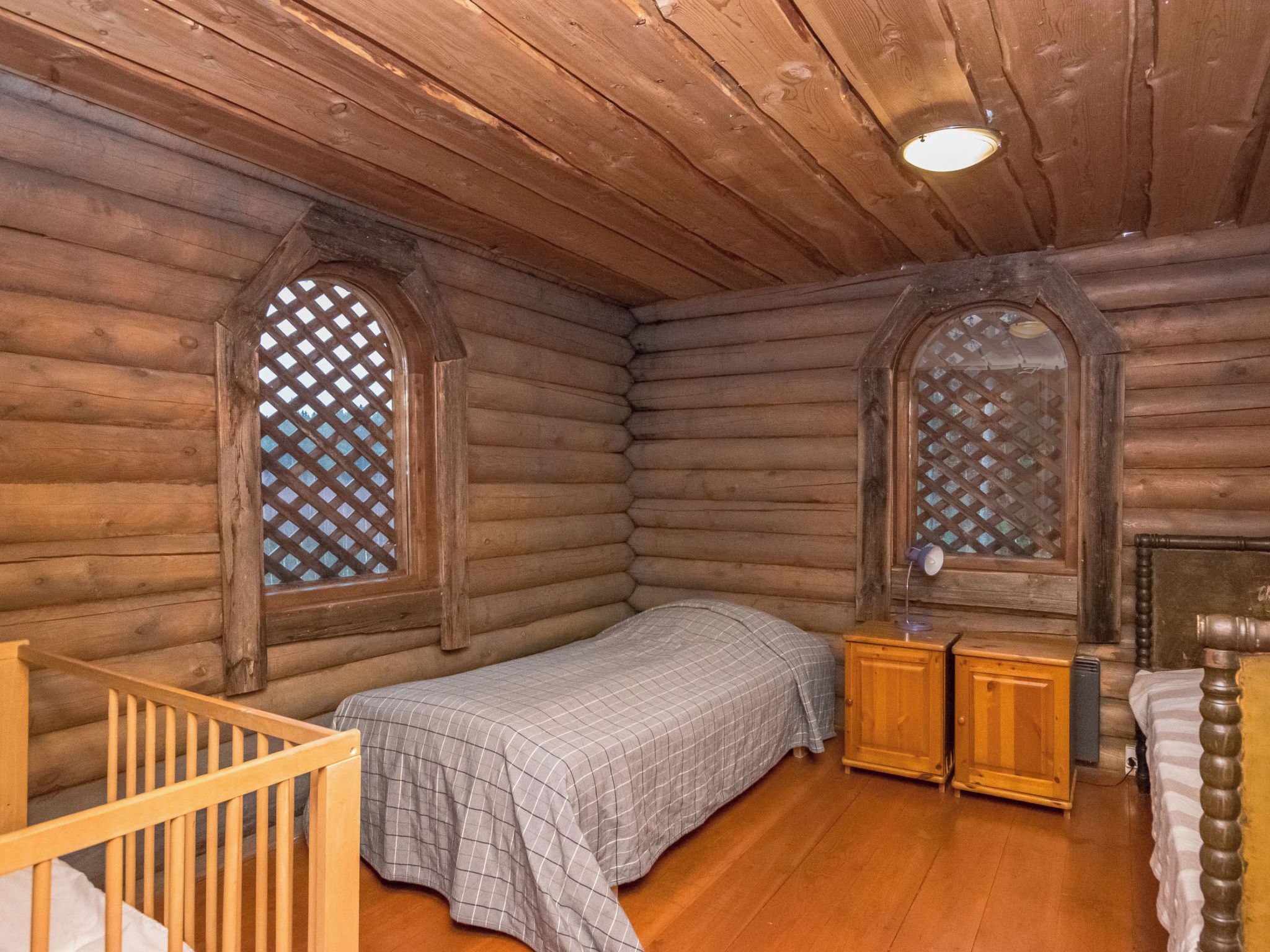 Ein Blockhauszimmer mit einem Bett, hölzernen Nachttischen und einem Babybett.