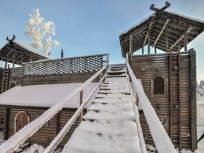 Een houten trap die leidt naar een blokhut met een sneeuwbedekte dak en een lattenwerkconstructie.