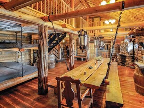 L’intérieur d’un chalet rustique en rondins de bois, avec une table à manger en bois, des bancs et des lanternes suspendues.