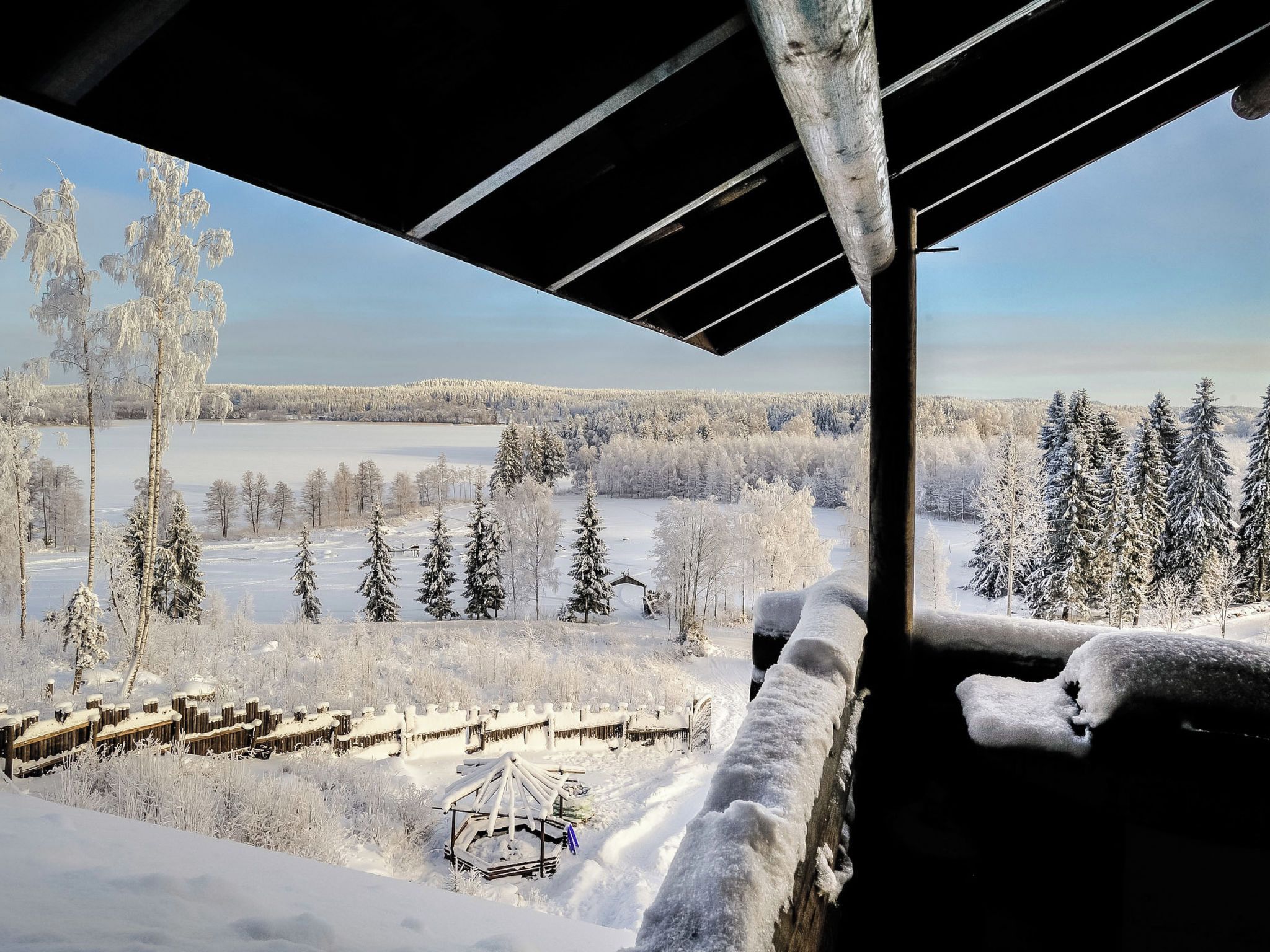 Lumipeitteinen maisema, josta avautuu näkymä metsään ja jäiseen järveen.