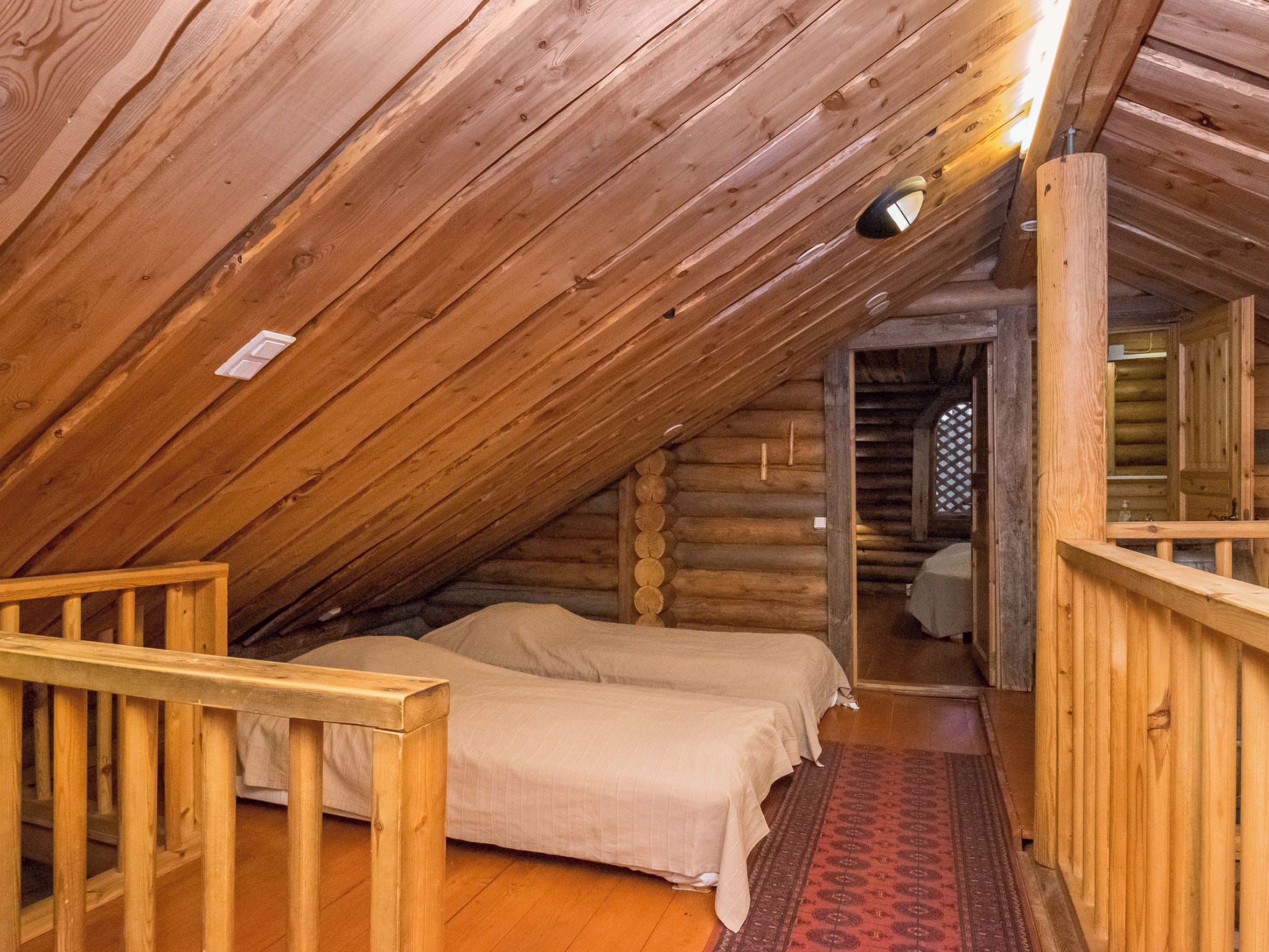Een blokhut met een slaapkamer op de zolder, met twee bedden, een houten leuning en een vloerkleed met dessin.