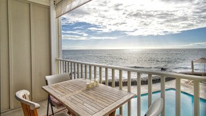 A balcony with a table and chairs overlooking a pool and the ocean.