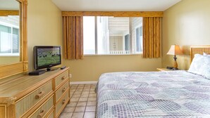 A hotel room with a bed, a television, a dresser, a lamp, and a window with curtains.