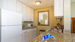 A kitchen with white cabinets, a granite countertop, a microwave, a kettle, and a sink.