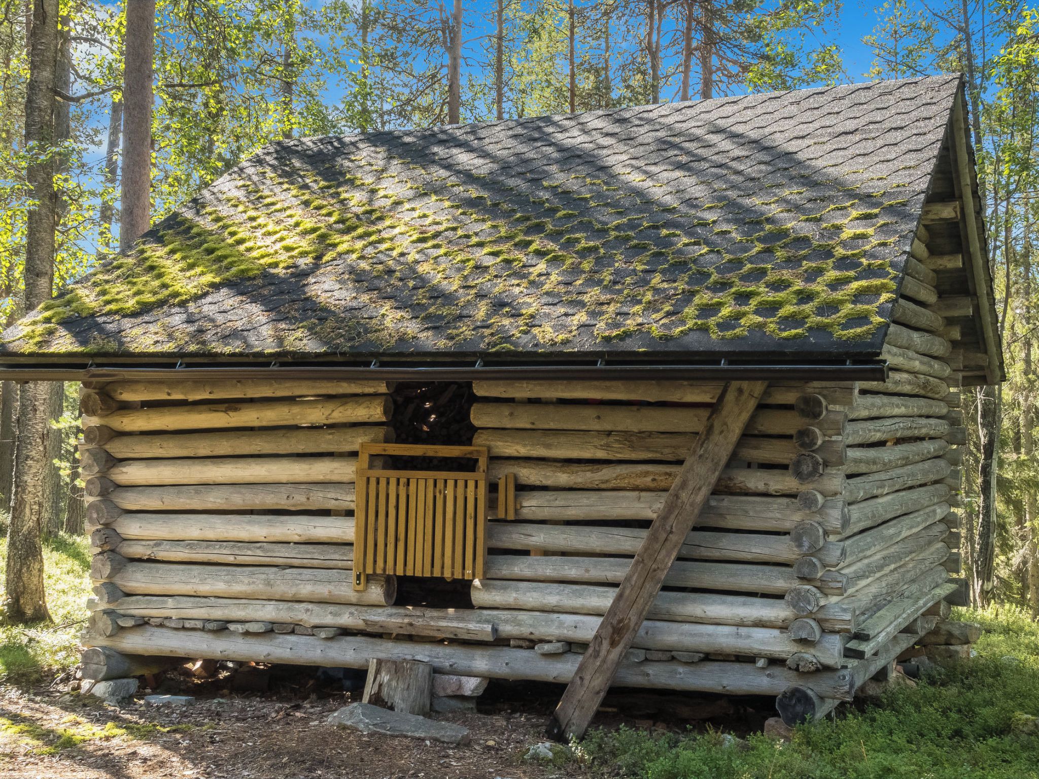 Hirsimökki, jossa on kalteva katto, puuovi ja ikkuna.