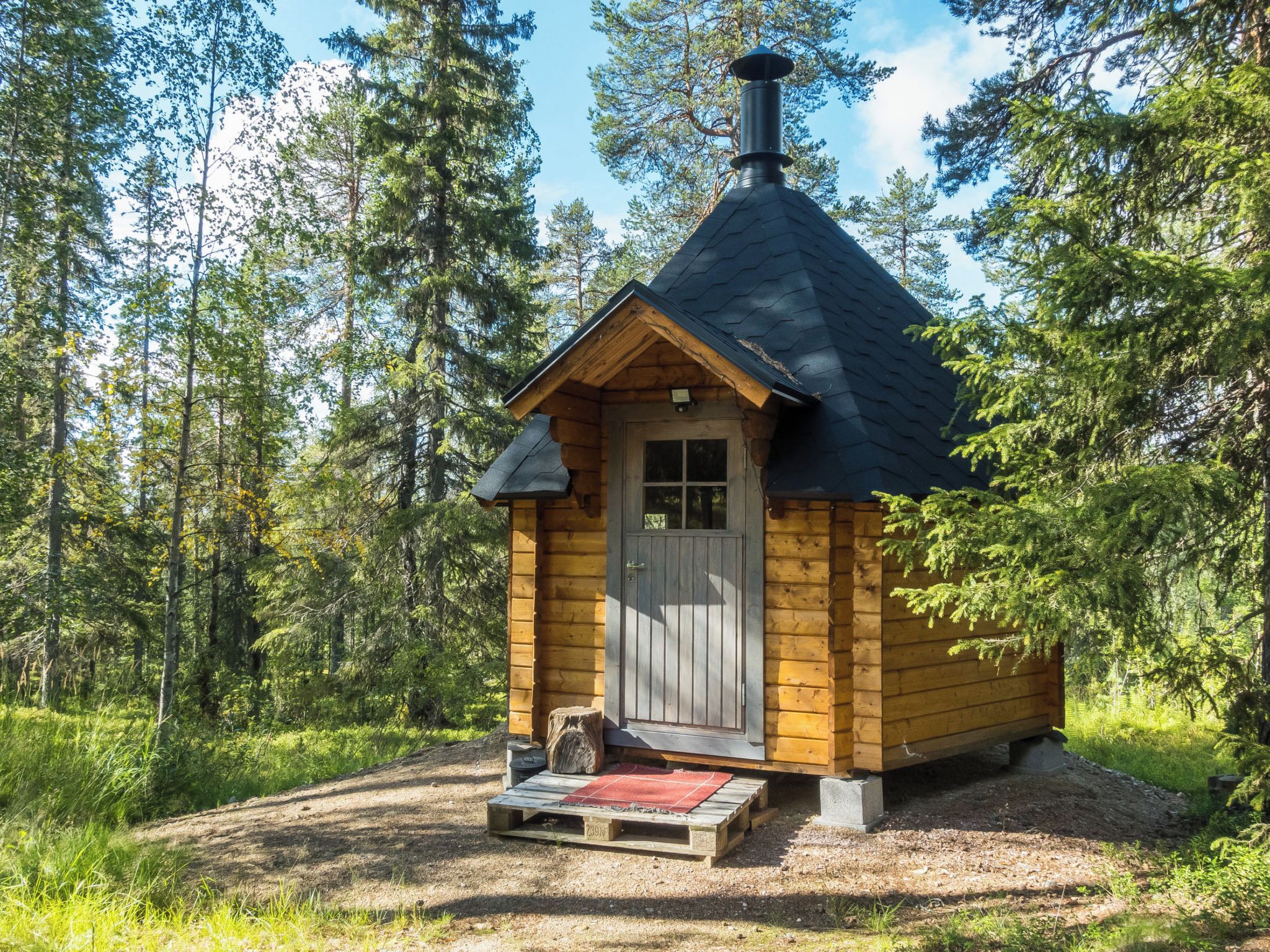 Una piccola casetta di legno con un camino, una porta e un piccolo portico con un tappeto.