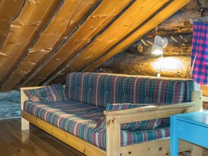 Une pièce mansardée chaleureuse, avec un plafond en pente en bois, un canapé à rayures, une petite table et une lampe.