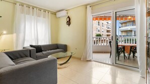 Ein Wohnzimmer mit grauem Sofa, einem Glastisch und einem Balkon mit Blick auf ein Gebäude.