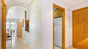 Ein Korridor mit einer Holztür, einem Kühlschrank und einem Essbereich mit Stühlen und einem Tisch.