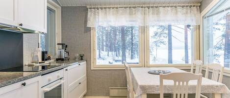 A modern kitchen with white cabinets, a built-in oven, and a window with a view of a snowy forest.