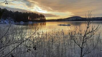 Rauhallinen näkymä järvelle auringonlaskun aikaan, tyyni vesi ja ympäröivät puut luovat idyllisen tunnelman.