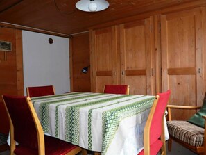 Ein Zimmer mit Holzboden, einem Tisch mit grün-weißer Tischdecke und Holzstühlen mit roten und grünen Kissen.