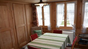 Ein Zimmer mit Holzwänden, einem für vier Personen gedeckten Tisch, zwei Stühlen und einem fenster mit Vorhängen.