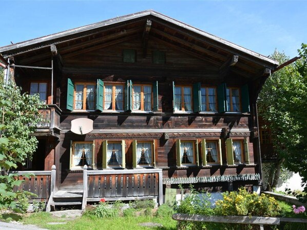 Ein traditionelles Holzchalet mit Balkon, mehreren Fenstern mit Fensterläden und einem Garten davor.