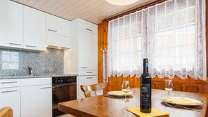 A modern kitchen with white cabinets, a granite countertop, and a wooden dining table with two chairs. - Almenrausch 1. OG Süd-Ost by Interhome (Riederalp)