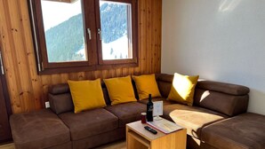 A cozy living room with a brown leather sofa, yellow cushions, a wooden coffee table, and a bottle of wine. - Almenrausch 1. OG Süd-Ost by Interhome (Riederalp)
