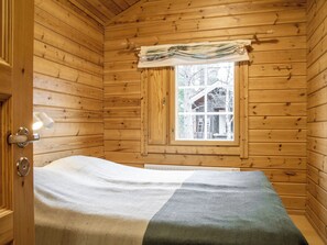 A wooden cabin room with a bed, a window, and a door.